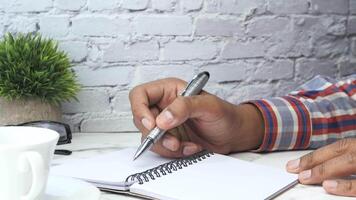 Man writing in notebook with pen on table video