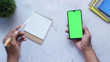 A person using a smartphone with a green screen and a notebook on a desk video