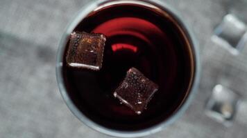 A glass of red wine with ice cubes in it video