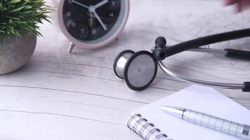 A stethoscope is next to a notepad and pen on a wooden table video