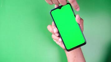 A hand holding a smartphone with a green screen on a green background video