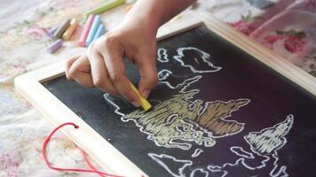A child drawing on a chalkboard with a world map video