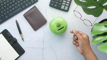 A person's hand is holding a green piggy bank on a desk with a laptop, pen video