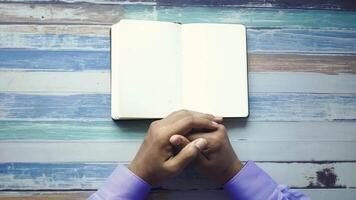 Hands of man praying in front of open book on wooden background video