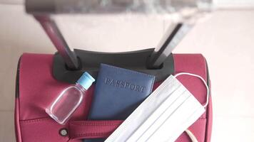A red suitcase with a passport, a bottle of hand sanitizer, and a mask video