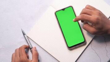 A man is using a smartphone with a green screen on a notebook video