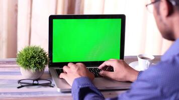 A man is typing on a laptop with a green screen video