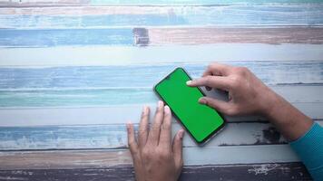 A person using a smartphone with a green screen on a wooden background video