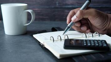 A man writing in a notebook with a pen and a calculator on a desk video