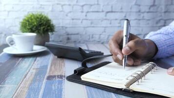 A man writing in a notebook on a desk with a cup of coffee and a pen video