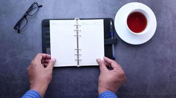 Top view of man's hands writing in notepad with pen and cup of tea on dark table video