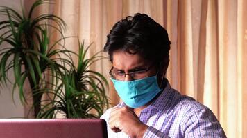 A man wearing a face mask while using a laptop video