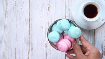 A person holding a bowl of colorful macarons next to a cup of coffee video