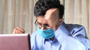 A man wearing a face mask while using a laptop video