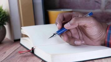 A man writing in a notebook with a pen on a wooden table video