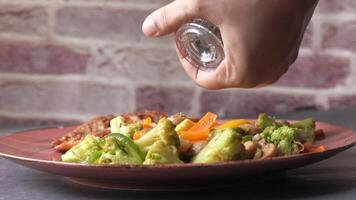 A person is holding a salt shaker over a plate of vegetables video