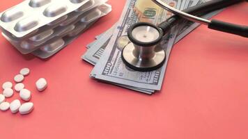 A stethoscope, pills and money on a pink background video