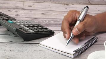 A person's hand writing on a notebook with a calculator and a cup of coffee video