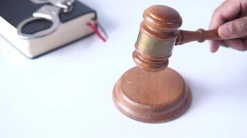 A judge's gavel is placed on a white table with a book and handcuffs video