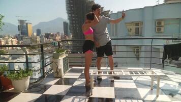 A couple joyfully taking a selfie on a rooftop with stunning city views in the background video