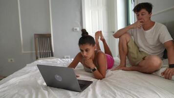 Young friends engaged with a laptop on a bed, enjoying digital interaction in a relaxed setting video