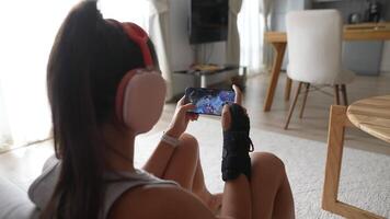 A girl is engaged in gaming while wearing headphones in her cozy living room setting video