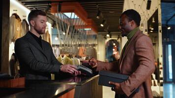 Black Man at Counter Buys Shoes from Friendly Retail Sales Assistant, Paying with Contactless NFC Smartphone Touching Terminal video