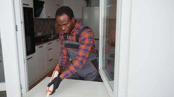 Worker with tube of sealant and suction lifters installing plastic windows indoors video