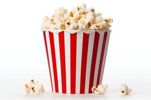 A red and white striped popcorn bucket is sitting on a white surface. The bucket is full of popcorn. There are some pieces of popcorn scattered around the bucket. photo