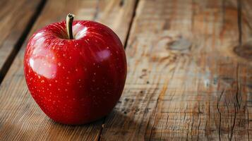 A single, shiny red apple sits on a wooden table. The apple is unblemished and perfect. photo