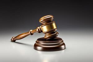A wooden judge's gavel resting on a sound block. The gavel has a gold band around the middle. photo