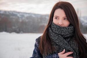 A woman with a thoughtful expression, wrapped in a thick gray scarf in a snowy field, conveying a sense of warmth and introspection. Reflects winter fashion and personal reflection photo