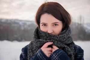 A woman wrapped in a large gray scarf, gazing into the distance with a calm expression, symbolizing warmth and serenity in a winter setting. Captures coziness and reflective moments photo