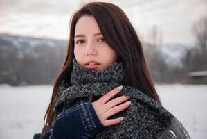 A woman in a grey scarf standing outdoors in a winter landscape, with calm expression, representing warmth and tranquility in the cold season photo