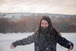 A joyful woman enjoying a snowy day with arms wide open, snow falling all around her in a serene outdoor setting. Freedom and happiness in winter photo