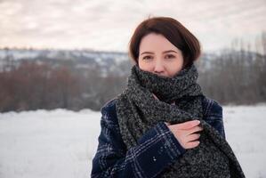 A woman in a plaid coat and thick scarf standing in a snowy field, with a serene and confident expression, representing winter elegance and warmth. Captures comfort and seasonal style photo