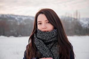 A close-up portrait of a woman wrapped in a plaid coat and thick scarf, gazing calmly into the distance, representing winter warmth and elegance. Highlights personal style and comfort photo