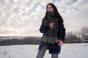 A woman wrapped in a thick scarf and plaid coat, looking over her shoulder with a playful smile, standing in a snowy field. Cozy winter fashion and playful attitude photo