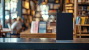 Black blank sandwich board on a counter in a cafe within a bookstore, with customers enjoying coffee and books. Empty sandwich board photo