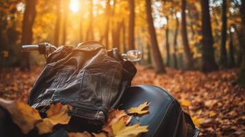Rugged leather jacket on a motorcycle seat surrounded by golden autumn leaves in a forest clearing, creating a contrast between textures. Autumn clothing photo