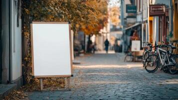 White blank sandwich board on a quiet street in a picturesque small town, placed outside a local artisan shop with bicycles and trees nearby. Empty sandwich board photo