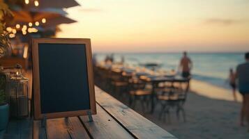Black blank sandwich board on a wooden deck at a seaside restaurant, with beachgoers and golden sunset in the background. Empty sandwich board photo