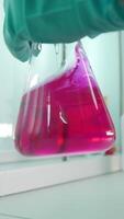 Close-up of flask with chemical liquid. Clip. Laboratory assistant conducts experiments with chemical liquid that changes colors. Chemical process in transparent flask in laboratory video