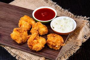 CRISPY COCONUT SHRIMPS with tomato sauce and mayo dip served on wooden board isolated on napkin side view of fast food on dark background photo
