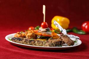 Assorted Mixed Grill Platter with Grilled Vegetables tikka boti seekh kabab of chicken, beef, lamb, mutton kebab and chops served in plate isolated on red background side view of arabic food photo