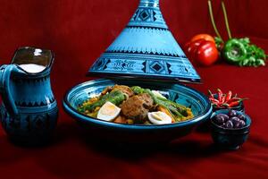 Tunisian Couscous fluffy grains topped with a flavorful stew of meat, vegetables, and spices served in pot isolated on red background side view of arabic food photo