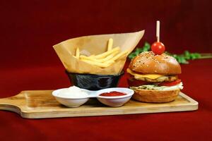 Chicken Burger and Fries topped with cheese, lettuce, and tomato served in wooden board with dipping sauce side view of fastfoods photo