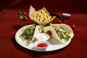 Savory Chicken Tacos with Fries filled with lettuce, and tomatoes are wrapped in warm tortillas topped with creamy avocado, ketchup and mayo dip isolated on red background top view of arabic food photo