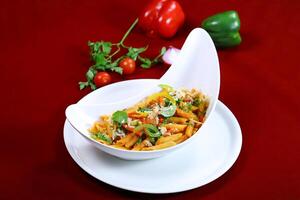 penne arrabiata pasta topping with coriander, capsicum and tomato sauce served in dish isolated on red background side view of italian food photo