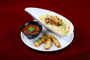 Classic Spaghetti Bolognese with Garlic Bread and featuring tender ground beef simmered in a rich tomato sauce served in plate isolated on red background side view of italian food photo